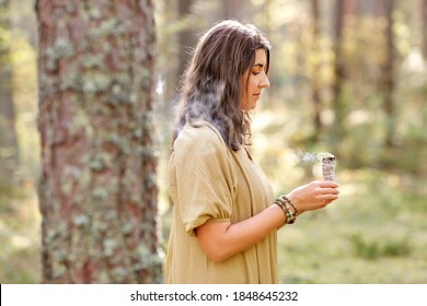 Occult Science And Supernatural Concept - Young Woman Or Witch With Smoking White Sage Performing Magic Ritual In Forest