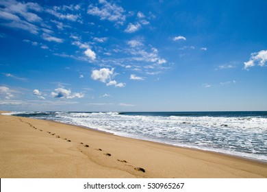 Ocean Beach With Footprints On Sand On Background Of Blue Sky