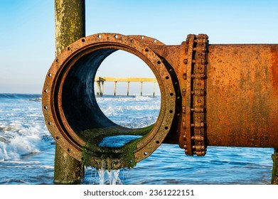 An ocean drain pipe with a pier in the background