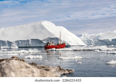 OCEAN ICEBERG WITH RED FISHING SHIP IN GREENLAND