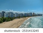 Ocean Park Beach, San Juan, Puerto Rico: golden sands meet ocean waves, lined with palm trees and modern beachfront buildings under a bright blue sky, creating a serene and tropical atmosphere. 