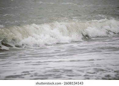 The ocean is rough and choppy, with a large wave crashing onto the shore. The water is a mix of white foam and gray water, creating a sense of movement and energy. The scene is dynamic and powerful