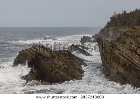 The ocean is rough and the rocks are jagged. The waves are crashing against the rocks, creating a powerful and dynamic scene. Scene is one of strength and resilience