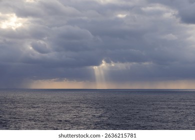 Ocean scape showing dramatic clouds and light rays over the Pacific Ocean at dusk.