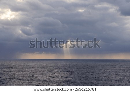 Ocean scape showing dramatic clouds and light rays over the Pacific Ocean at dusk.
