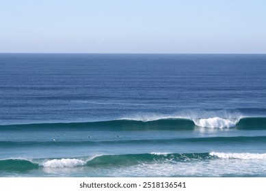 Ocean scene with gentle waves rolling in toward the shore. Several surfers preparing to catch the next wave. The ocean and sky above is clear and calm, with space for copy. - Powered by Shutterstock