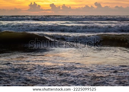 Ocean sea waves coming to shore with white foam bubbles.color reflection of a yellow sky visible on the water surface -  Sri Lanka