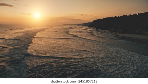 Ocean seascape at sunset light with cliff coast silhouette aerial view. Dark rock sea shore, sand beach of Sumba Island, Indonesia. Nobody nature scape of tropic paradise resort. Cinematic drone shot - Powered by Shutterstock