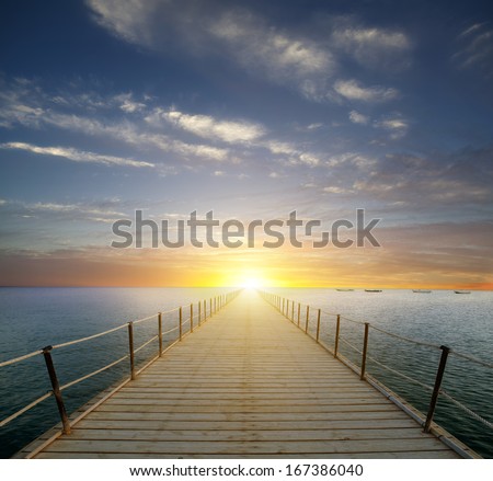 ocean sunrise with pier and beach in foreground 