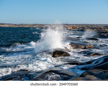 Ocean wave crashes into cliffs in a storm. Big splash and white foam. Rocky background. No visible people.