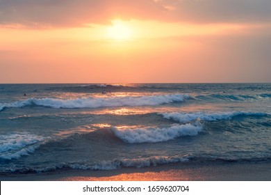 Ocean waves and beautiful sunset sky over horizon. Surfers floating on waves in expectation.