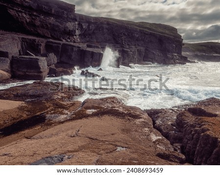 Ocean waves crushing on rough stone coast of rugged Irish coast line with cliffs. Kilkee area, Ireland. Popular travel and tourism area with stunning nature scenery. Dramatic cloudy sky.