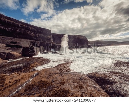 Ocean waves crushing on rough stone coast of rugged Irish coast line with cliffs. Kilkee area, Ireland. Popular travel and tourism area with stunning nature scenery. Dramatic cloudy sky.
