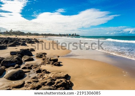 Ocean waves and sandy beach on a sunny day. Nature tropical background. Low tide with rocks exposed at Kellys Beach, Queensland, Australia