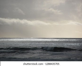 Ocean waves under a cloudy sky with light areas streaking the water.  
