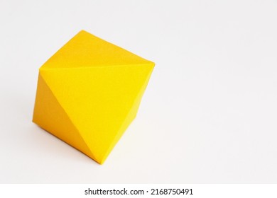 An octahedron or rhombus in intense yellow cardboard on a white background seen from a high angle.