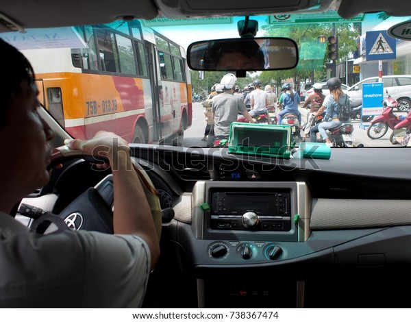 October 13, 2017, inside a taxi meter driver wearing\
white shirt driving in a world cultural heritage HUE city of\
VIETNAM on rush hour with busy and hurry people on the street in\
front of the vehicle 