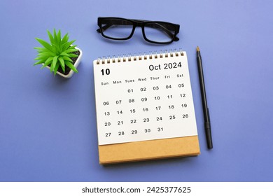 October 2024 desk calendar with potted plant, pen and reading glasses on blue background. - Powered by Shutterstock