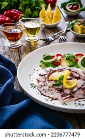 Octopus carpaccio with lemon and greens on wooden table 