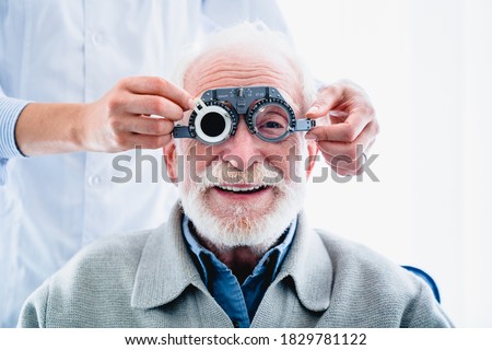 Oculist putting ophthalmic glasses on smiling elderly male patient