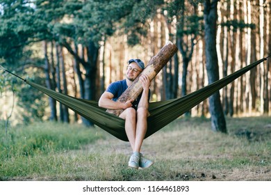Odd weird strange unusual male person. Outlandish funny crazy foolish man sleeping in hammock with huge wooden log at nature among trees.  Wood and forest lover. With beam in bed.  Leisure lifestyle