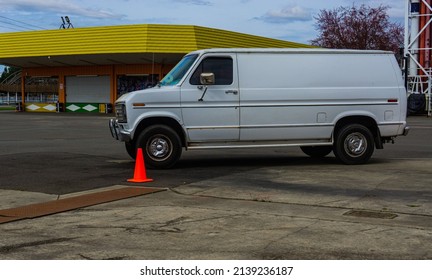 Odd white van sitting in the middle of a cement open area.