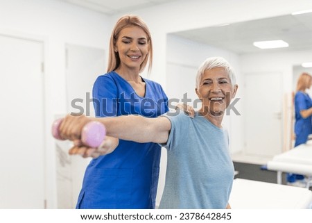 Oder aged woman doing physiotherapy with support from physiotherapists . Senior elderly female sitting in clinic using dumbbells workout exercise for patient with caregiver in nursing care.
