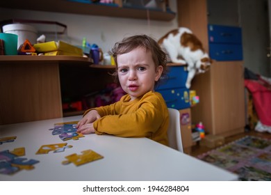 Odessa, Ukraine - 01.08.2020 Little Girl In Mustard Pajamas Sits At The Table, Collects Puzzles. Frustrated Child Is Sad That The Puzzle Doesn't Fit. Ginger Cat Walks Around The Room. Concept Of Logic