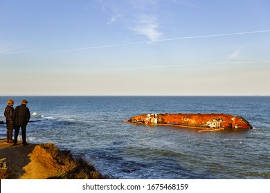 Odessa / Ukraine - 02.26.2020: An Elderly Couple Is Looking From The Hill At The Shipwrecked Tanker That Lies In The Sea Near Dolphin Beach