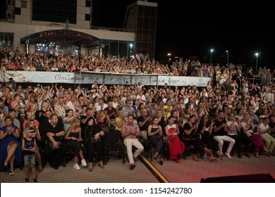 Odessa, Ukraine August 4, 2018: Rear View Of Crowd With Arms Outstretched At Concert. Silhouettes Of Concert Crowd In Front Of Bright Stage Lights. Crowd At Music Concert, Audience Raising Hands Up