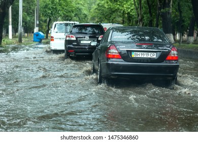 Odessa, Ukraine -August 9,2019: driving car on flooded road during flood caused by torrential rains. Cars float on water, flooding streets. Splash on the car. Flooded city road with a large puddle - Shutterstock ID 1475346860