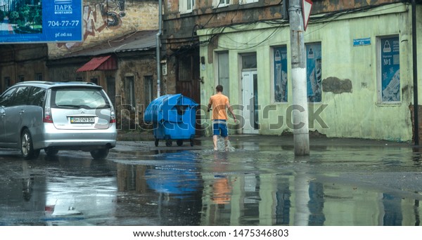 Odessa, Ukraine -August 9,2019: driving car on\
flooded road during flood caused by torrential rains. Cars float on\
water, flooding streets. Splash on the car. Flooded city road with\
a large puddle