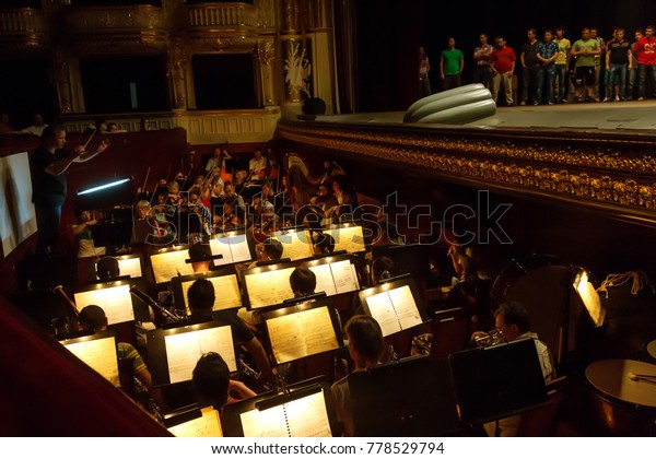 ODESSA,\
UKRAINE - July 3, 2013: Orchestra pit with director, notes, musical\
instruments and performers performing at the National Theater of\
Opera and Ballet. The score on the music\
stand
