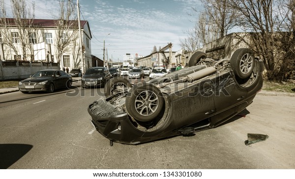 ODESSA, UKRAINE March 19, 2019: after car accident,\
broken car rolled over and lay down on roof on road that other cars\
drive. Concept of careless driving, breaking rules and speeding on\
road