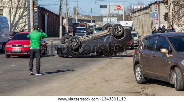 ODESSA, UKRAINE March 19, 2019: after car accident,\
broken car rolled over and lay down on roof on road that other cars\
drive. Concept of careless driving, breaking rules and speeding on\
road