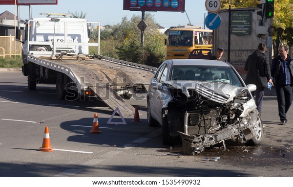 ODESSA, UKRAINE - October 16, 2019: Car accident,\
head-on collision. A tow truck loads a wrecked car after an\
accident. Traffic police officer during an investigation in a\
traffic accident zone