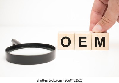 oem text wooden cube blocks and hand holding magnifying glass on table background.