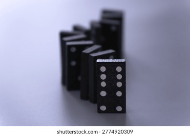 An off centered vertically aligned row of dominoes on a white surface in a s curved pattern
