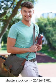 Off to class. A handsome student standing outside on campus with a satchel and a textbook.