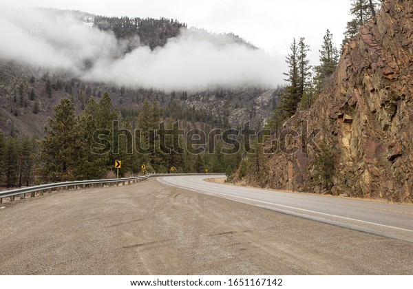 Off the highway before it rounds\
a corner with tree and fog covered mountain on overcast\
day