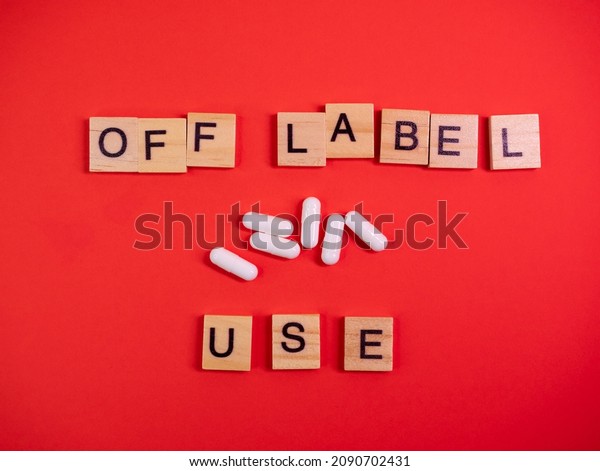 Off label approved medicine pill use. Covid-19
therapy. Words off label and white capsules or pill drugs on
colored red paper texture background. Pharmacy concept. Copy space.
Mock up design template