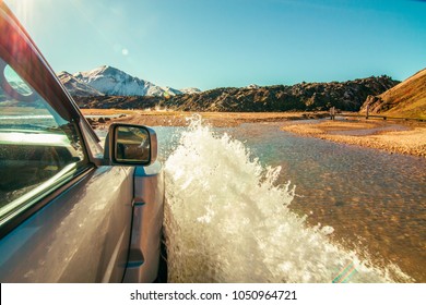 Off road action adventure traveler, 4 wheel drive 4x4 driving with a big splash through water in the Iceland, snow covered mountains in the background, blue sky