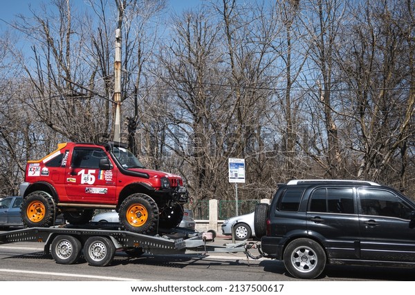 Off road racing car, towed by\
another car, on a car platform. Romania, Targu Jiu. March 17,\
2022