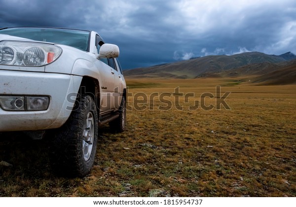 Off road suv car on moutain plateau with\
mountains and rain clouds background. Summer vacation, travel\
concept. Borokhudzir plateau, tourism in Kazakhstan concept.\
02.08.2020 Zharkent,\
Kazakhstan.