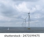 Off shore wind mills or turbines with large propellor blades turning in the wind in a lake in the Netherlands generating renewable green energy or electricity