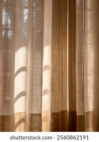 A off white curtain with a pattern of lines and dots. The curtain is hanging in front of a window, and the sunlight is shining on it, creating a shadow. The image has a warm and cozy feeling