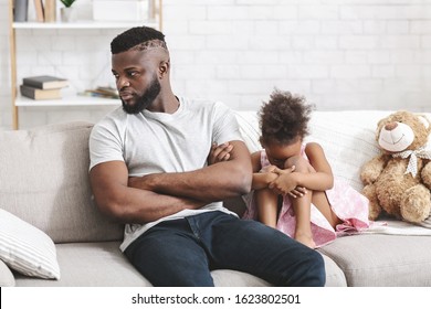 Offended black little girl crying, sitting on sofa next to angry dad, family conflict, home interior