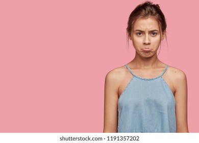 Offended Caucasian girl with insulted expression, scowls face, puses lips in discontent, has appealing look, dressed in casual clothes, poses over pink background, copy space for your advertisement - Shutterstock ID 1191357202