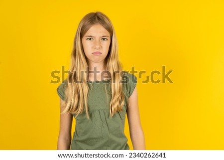 Offended dissatisfied Caucasian kid girl wearing green T-shirt over yellow background with moody displeased expression at camera being disappointed by something