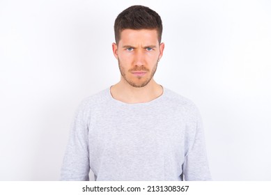 Offended dissatisfied young caucasian man wearing grey sweater over white background with moody displeased expression at camera being disappointed by something